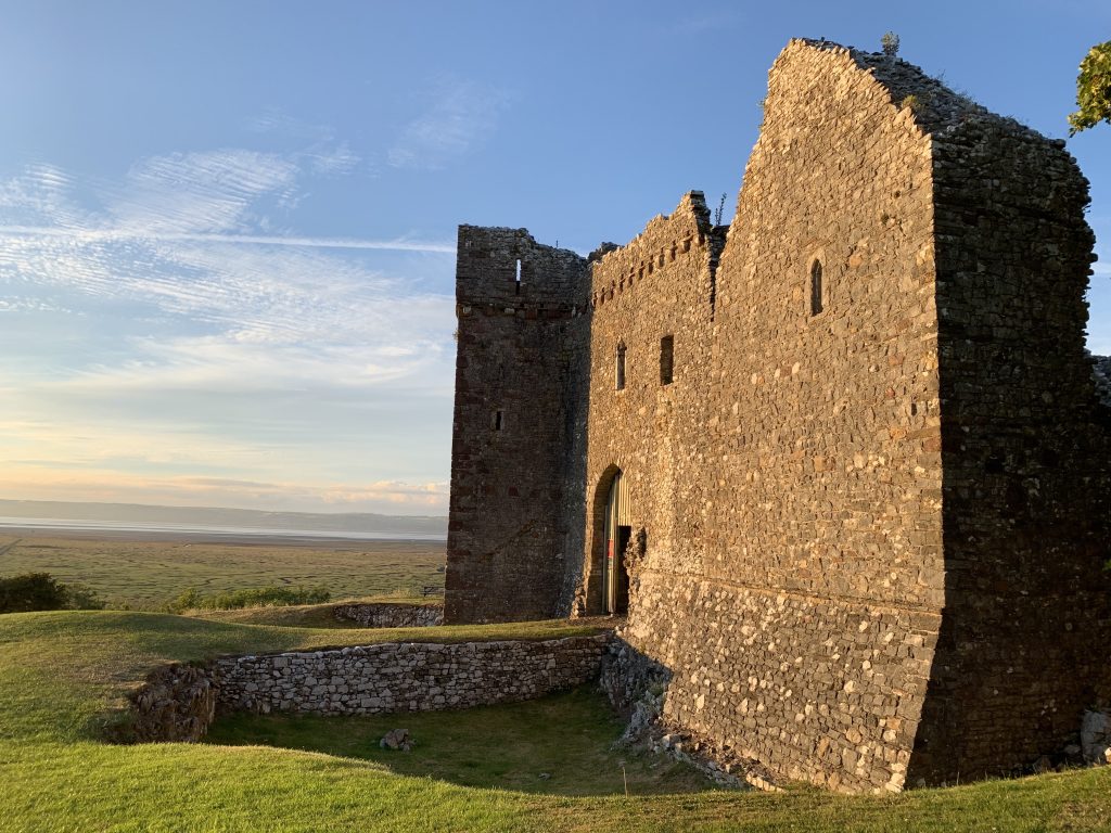 A view of the ruins of Weobley Castle as the sun is setting, with the Gower Peninsula in the background 