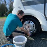 A man kneeling down cleaning the wheels of a Motorhome