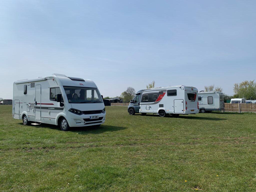 3 motorhomes are parked up on a large grass field in a Campsite