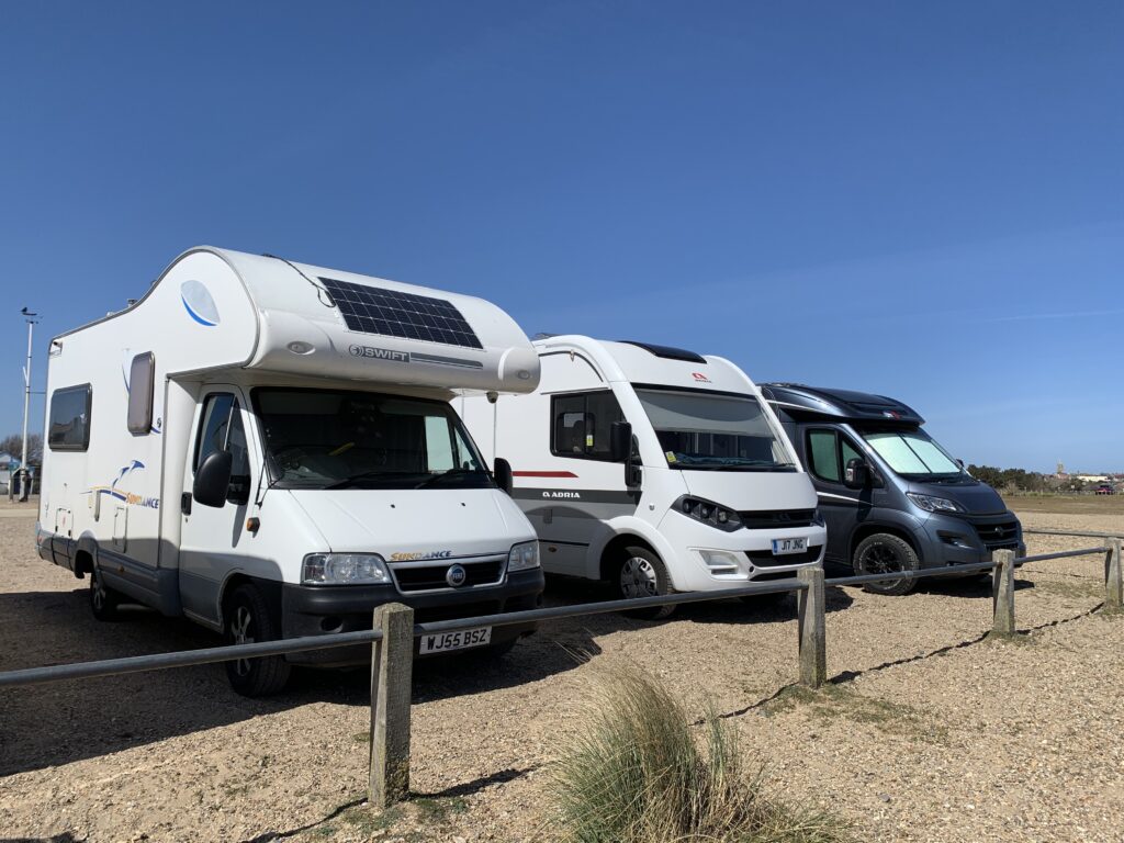 3 motorhomes are parked in a gravel car park, overlooking the beach