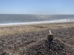 A small Sandcastle sits atop a mound of stones on a beach. There is a row of stone which leads to sand and then on to the water