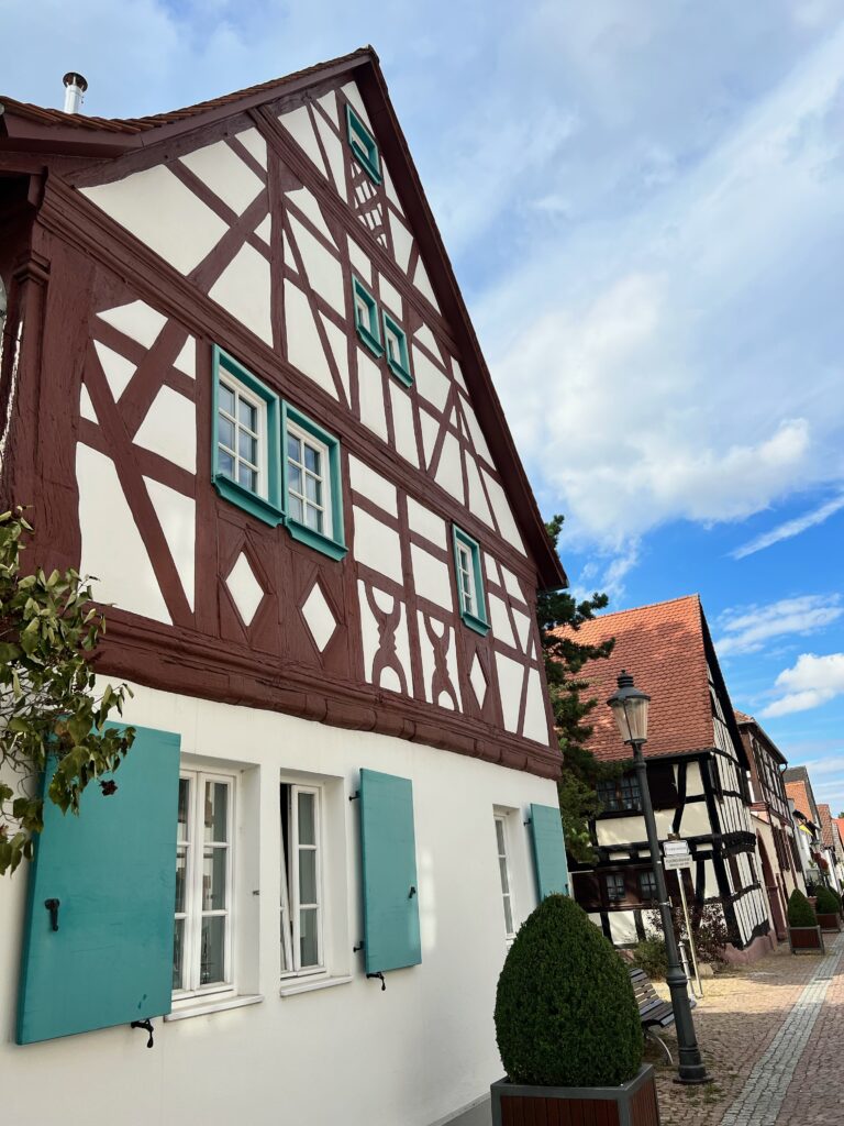 the picture shows a typical looking German house, white with a triangle roof, brown wooden fronting and green window shutters