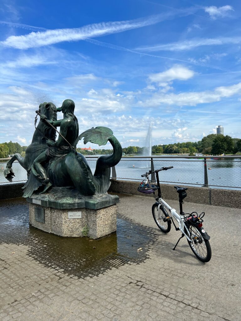A folding bike is stood up next to a statue overlooking the river in the city of Nuremberg