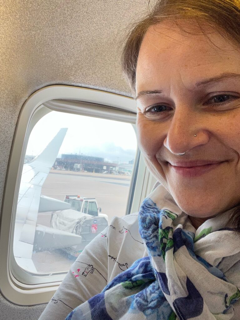 a lady smiles for a selfie infant of the windows of an aeroplane