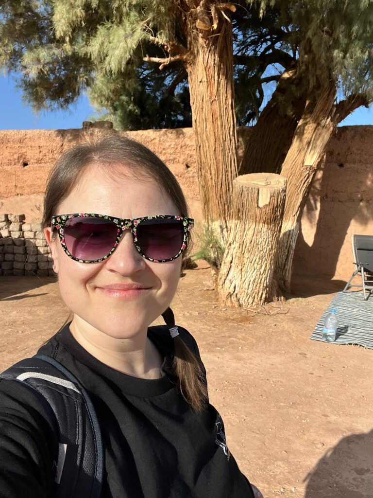 A lady is taking a selfie, smiling stood at a campsite in Morocco