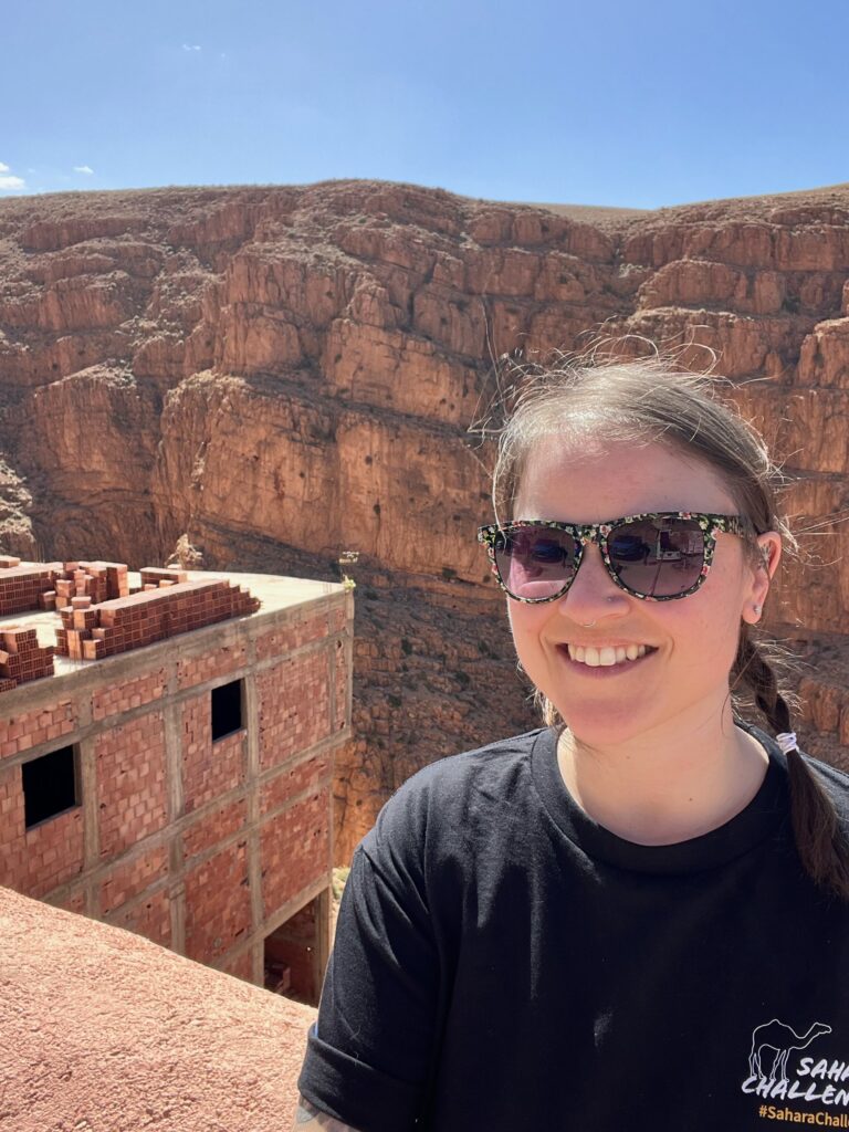 A lady takes a selfie at the view point form the top of the Dades Gorge, behind her you can see an unfinished building and the huge rock formation