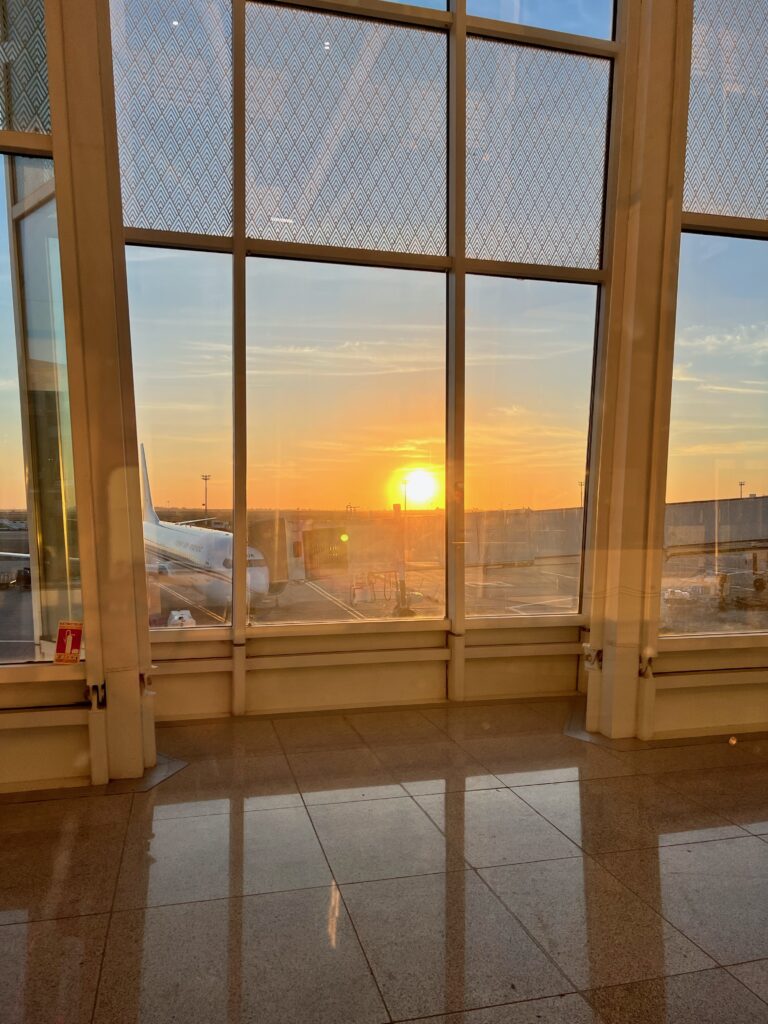 The view if from inside Casablanca airport, looking out over a plane waiting at the terminal with the sun setting in the background