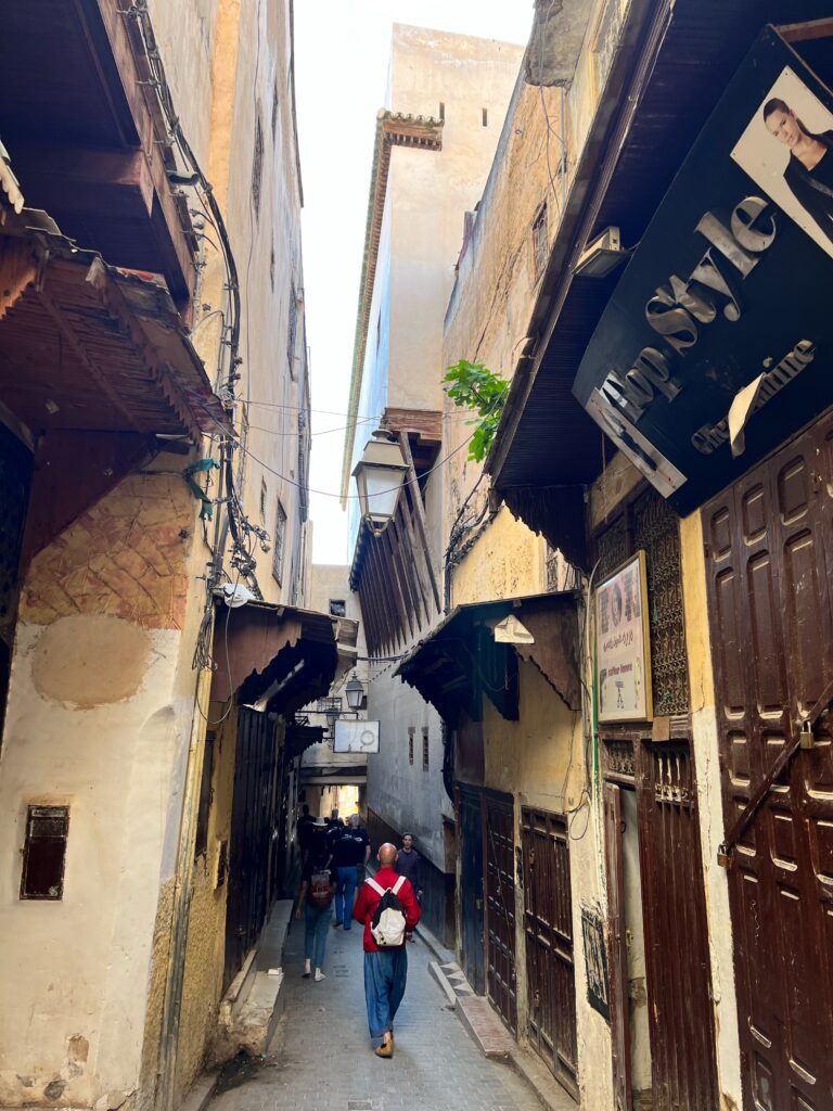 A group of people are walking down the quiet, narrow streets of the Medina de Fez