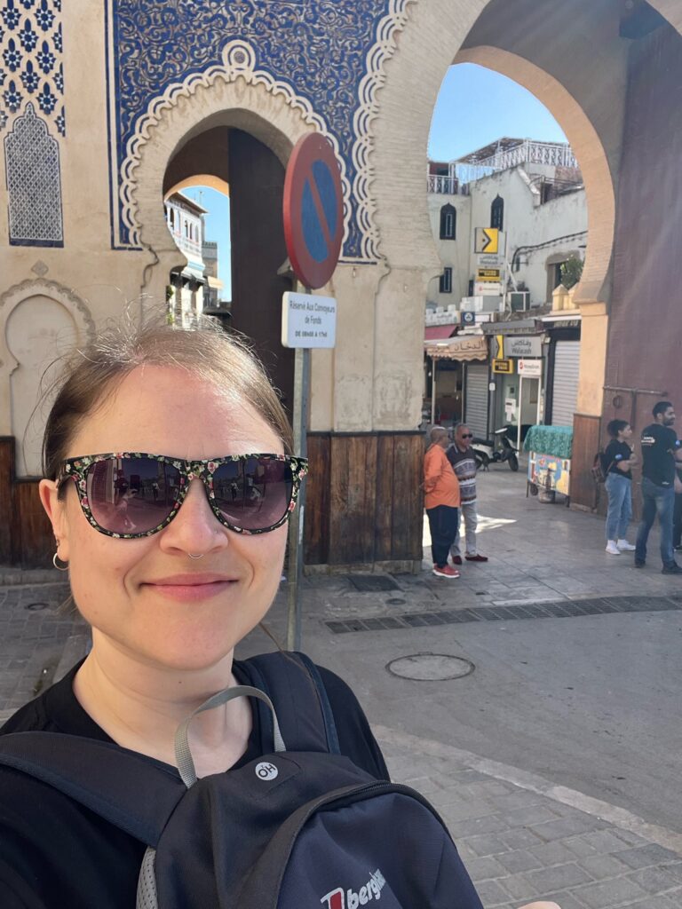 a lady stands smiling for a selfie outside the blue gate, the grand entrance to Medina de fez