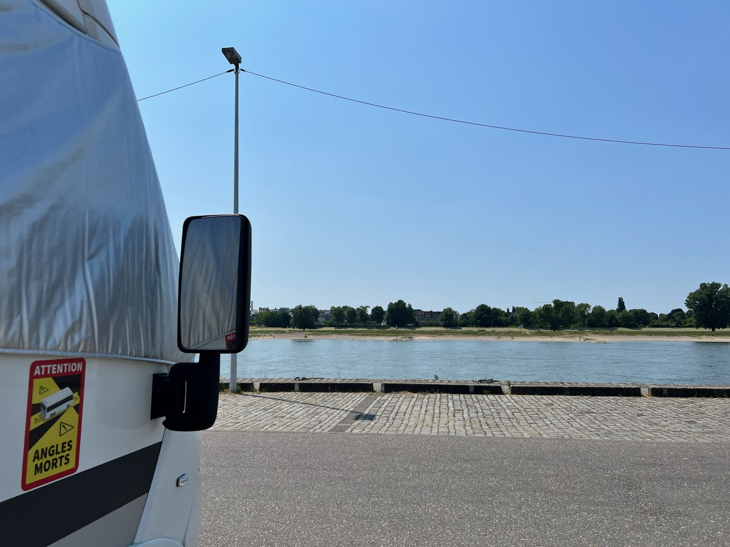 A motorhome is parked along the river front in Dusseldorf, the view is of a clear sunny day overlooking the water